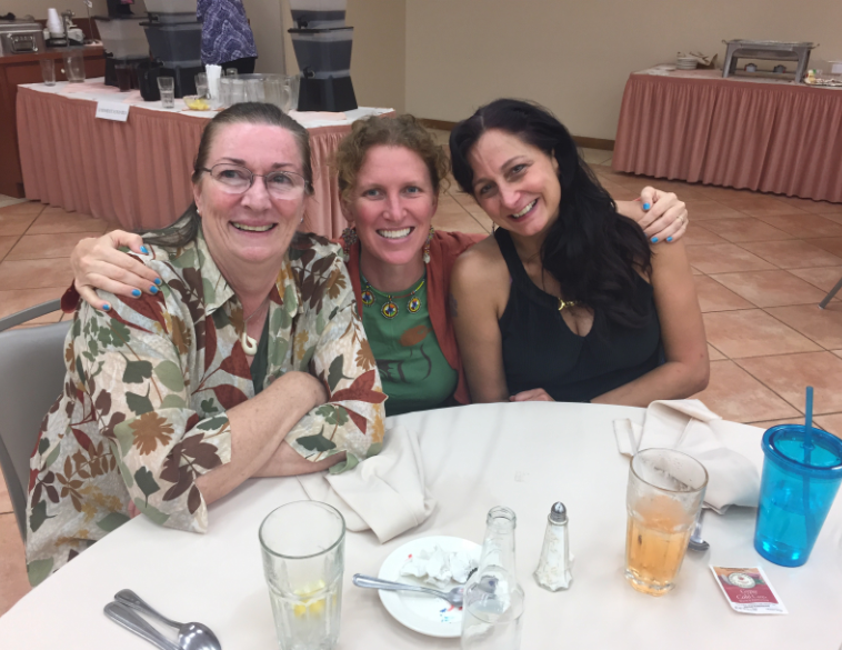 Three women sit arm in arm at a dining table at the Florida wildlife rehabilitation conference.