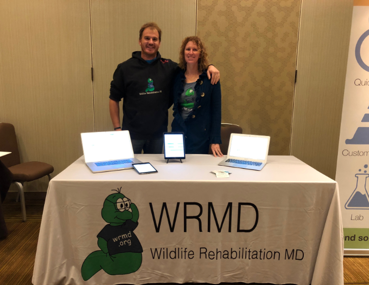 Two members of the WRMD team at their Wildlife Rehabilitation MD exhibit table, set up with laptops and tablets.