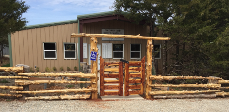 Metal-sided building behind a rustic log fence and a red wooden gate.