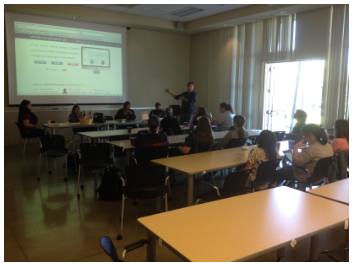A presenter stands beside a projected web page while wildlife rehabilitators listen from classroom tables.