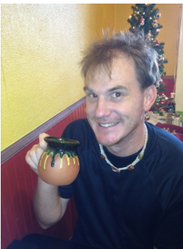 Devin smiling and holding up a small painted clay pot.
