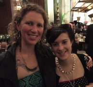 Two smiling women posing together at a crowded indoor gathering.