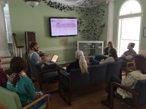 Wildlife rehabilitators seated in a sitting room, watching a presentation on a wall-mounted screen.
